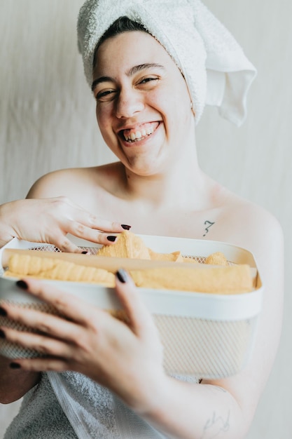 Woman holding basket with different shower supplies Hands with bright yellow and rolled up towels Metal mesh storage white basket Preparing products for a relaxing bath