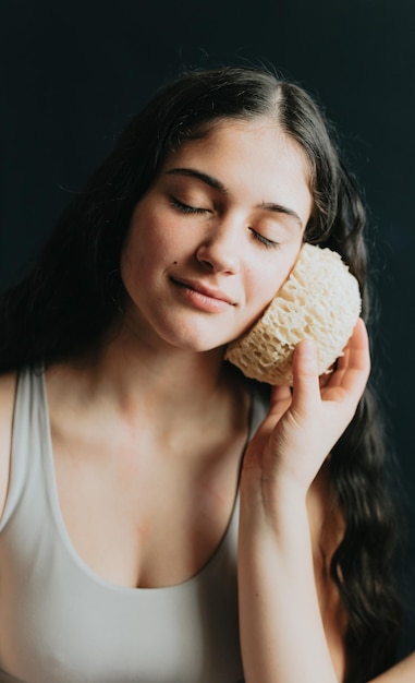 Woman holding a bath sponge Resting and using a sponge as a pillow after a shower Young adult wrapped in white towel personal hygiene and positive body care and selfcare