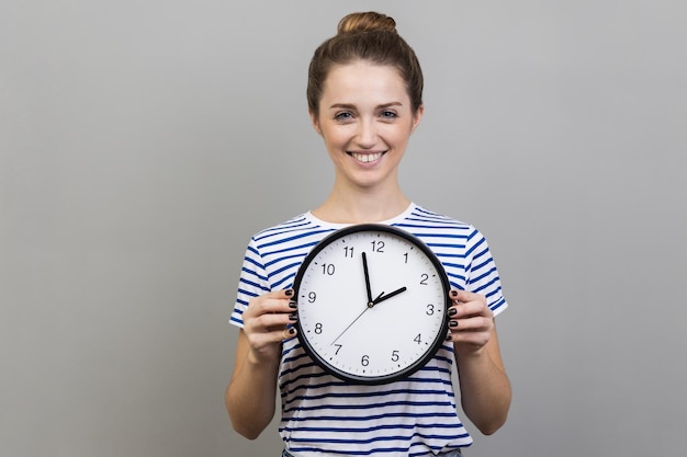 Woman holding big wall clock has satisfied expression being glad with completed work