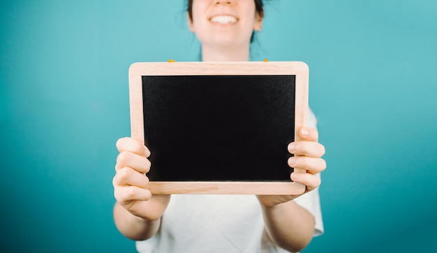 Woman holding a black board with blank space copy space for your text to camera while smiling happily Mock up scene concept Add your own text or image Color background minimal concept