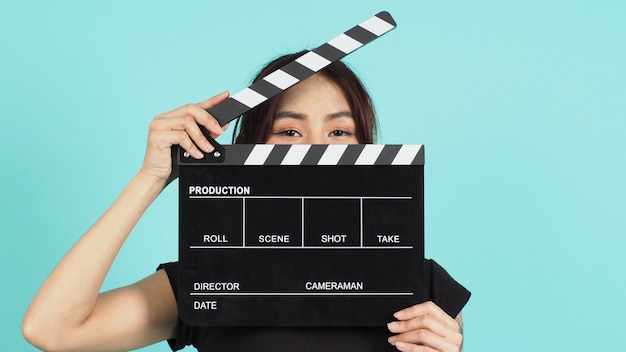 Woman holding black clapperboard or movie slate use in video production ,film, cinema industry on green mint or Tiffany Blue  background.