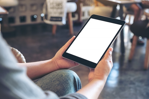  a woman holding black tablet pc with blank white screen while sitting in cafe