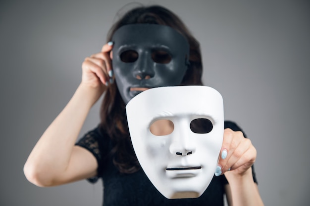 Woman holding black and white plastic mask on gray background