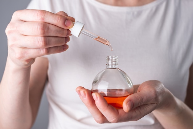 Woman holding a bottle of aromatic oil and a drop falling from the pipette