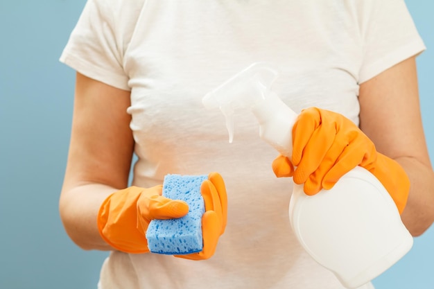 Woman holding a bottle of washing liquid and a sponge on a blue background