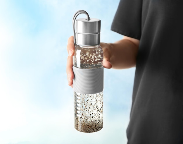 Woman holding bottle of water with chia seeds on light background