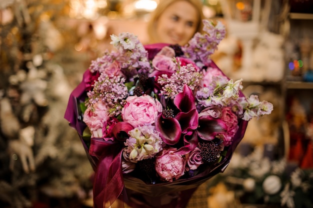 Woman holding a bouquet with pink, violet and crimson flowers wrapped in dark color paper