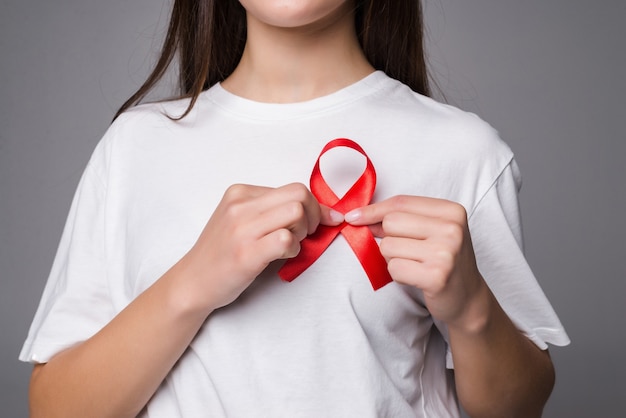 Woman holding breast with pink ribbon over white wall. Concept photo to support breast cancer cause. PS: you can change the pink ribbon into red for AIDS support cause.