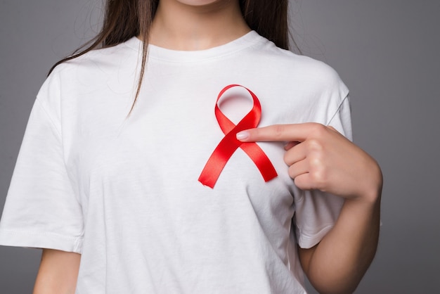 Woman holding breast with pink ribbon over white wall. Concept photo to support breast cancer cause. PS: you can change the pink ribbon into red for AIDS support cause.