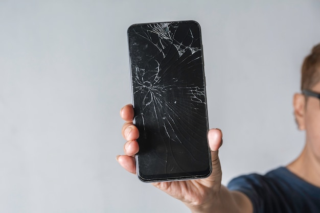 Woman holding a broken touch screen of smart phone on grey background.