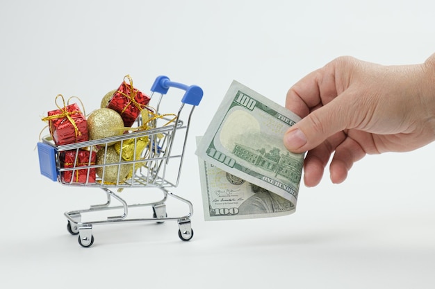 Woman holding cash dollars in front of the rolls full of Christmas gifts and Christmas decorations little shopping cart