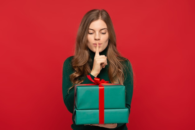 Woman holding Christmas gift and showing silence sign