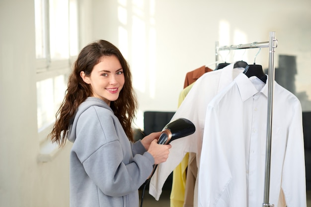 Woman holding compact hand steamer and washing white shirt at home