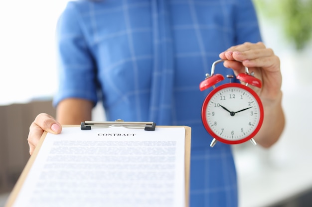 Woman holding contract and red alarm clock in her hands closeup schedule of working hours