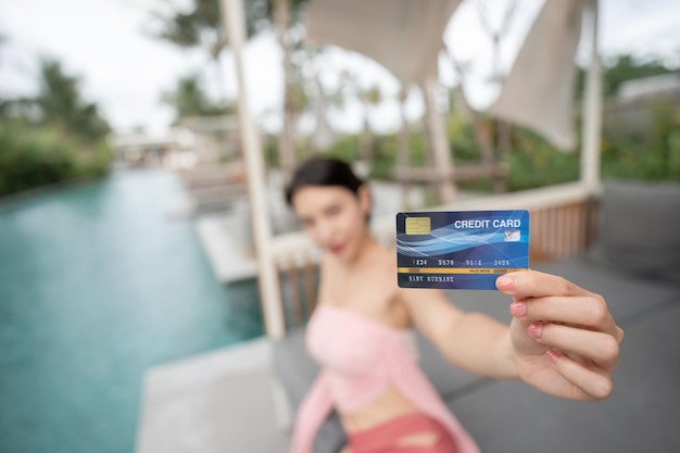 Woman holding credit card in hand by the pool shopping online on vacation