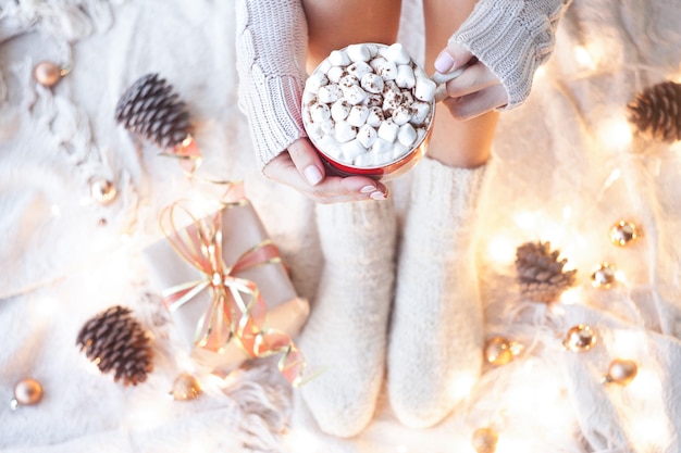 Woman holding a cup of cocoa with marshmallows on a bed with Christmas ornaments