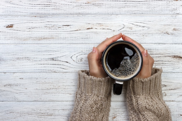 Woman holding cup of hot coffee on rustic wooden table