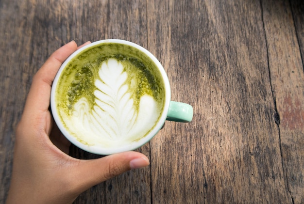 woman holding a cup of hot green tea latte on wooden table background. top view.