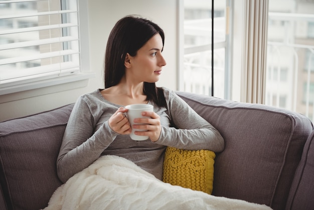 Woman holding cup while looking through window