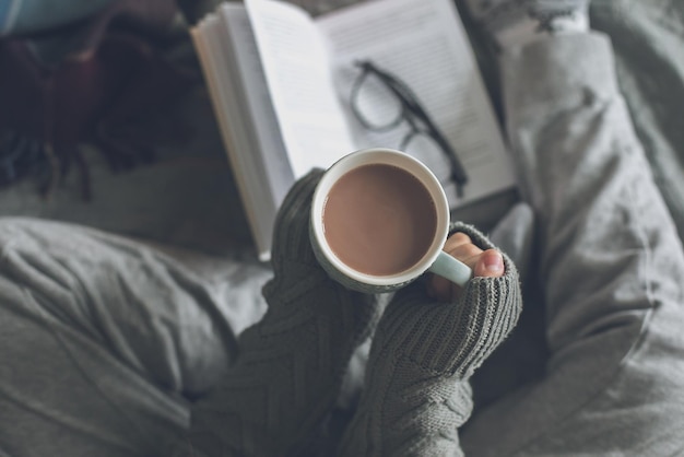 Woman holding cup with cacao or coffee reading book Concept of cozy home comfort leisure