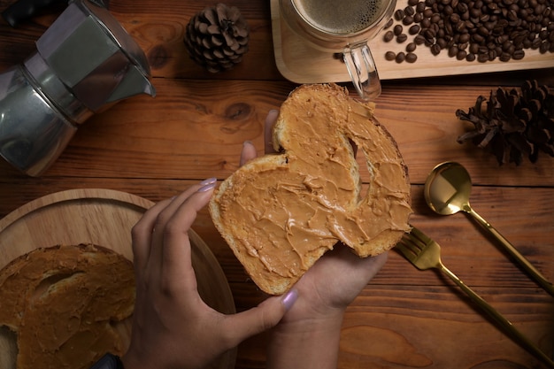 Woman holding delicious toast with peanut butter on wooden table.