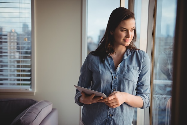 Woman holding digital tablet while looking through window