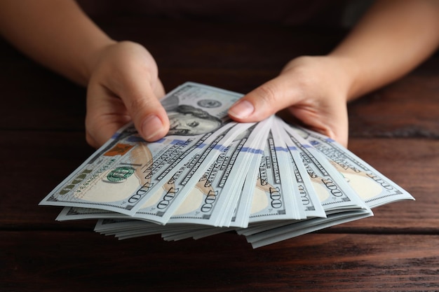 Woman holding dollar banknotes at wooden table closeup