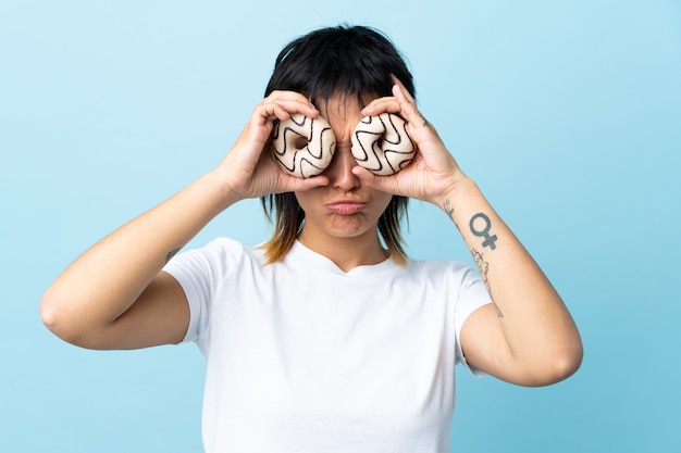 Woman holding a donut over blue wall