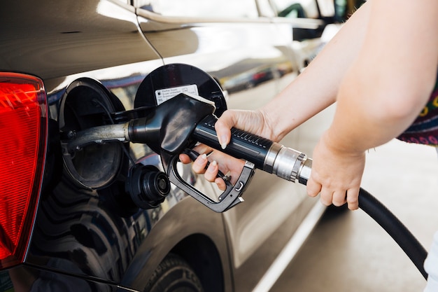 Woman holding filling gun in hands and fueling car