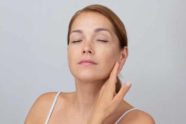 Woman holding fingers on cheek with closed eyes showing soft skin on white background