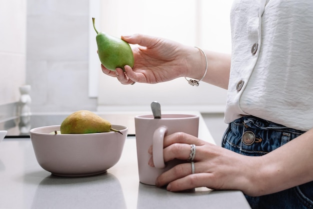 Woman holding fresh ripe pear in kitchen