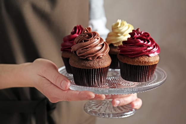 Woman holding glass stand with tasty chocolate cupcakes close up