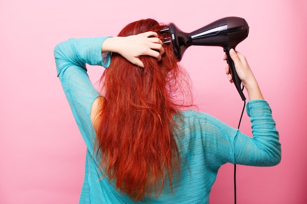 Woman holding a hairdryer on a pink background