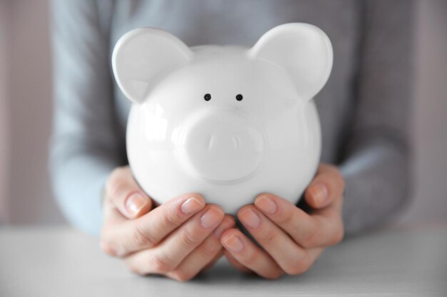 Woman holding in hands white piggy bank at the table