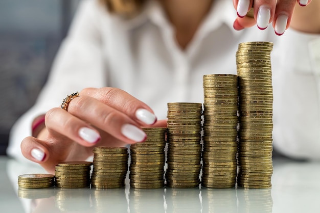 Woman holding her hands near a mountain of coins at a table or in front of stacks of coins