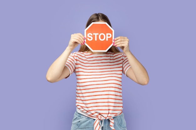 Woman holding and hiding her face with red stop sign attention to safe road crossing