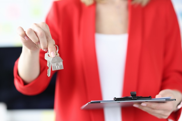 Woman holding house keys and clipboard with documents in her hands closeup real estate on