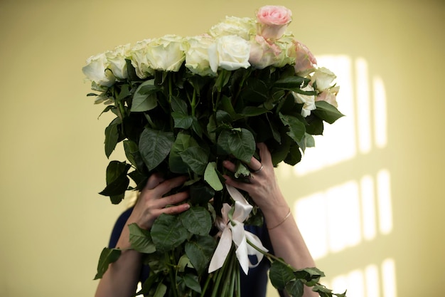 Woman holding a huge bouquet of white roses flowers covering her face