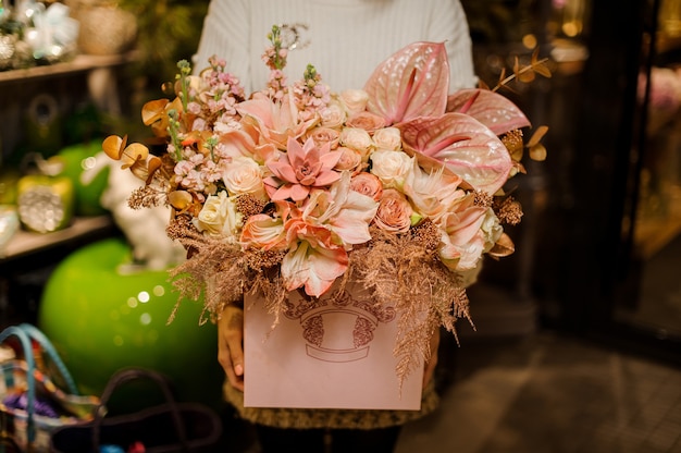 Woman holding a huge box of bright pink color roses, succulets and callas with golden decor