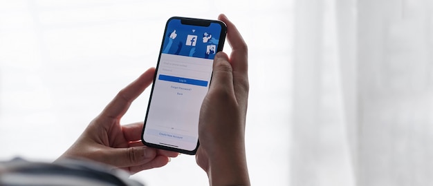 Woman holding a iPhone with social Internet service Facebook on the screen.