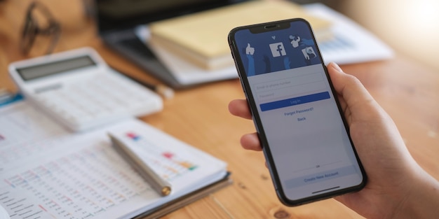 Woman holding a iPhone X with social Internet service Facebook on the screen.