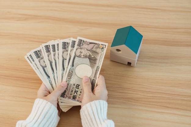 Woman holding Japanese Yen banknote and House model Real Estate Home Mortgage Japan cash Tax Recession Economy Inflation Investment finance and savings concepts