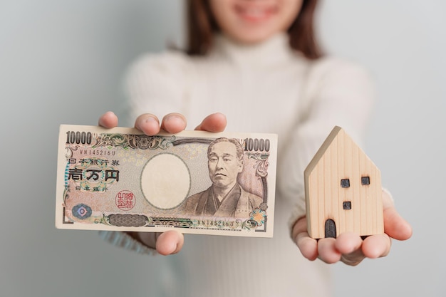 Woman holding Japanese Yen banknote and House model Real Estate Home Mortgage Japan cash Tax Recession Economy Inflation Investment finance and savings concepts