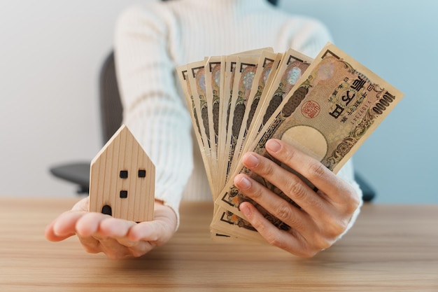 Woman holding Japanese Yen banknote and House model Real Estate Home Mortgage Japan cash Tax Recession Economy Inflation Investment finance and savings concepts