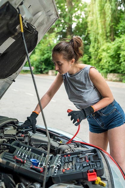 Photo woman holding jumper cable for recharge the battery car for repairing broken car service at outdoor