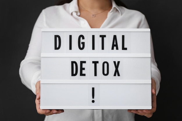 Woman holding lightbox with phrase DIGITAL DETOX on black background closeup