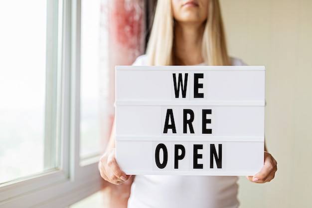 Woman holding lightbox with text we are open in hands