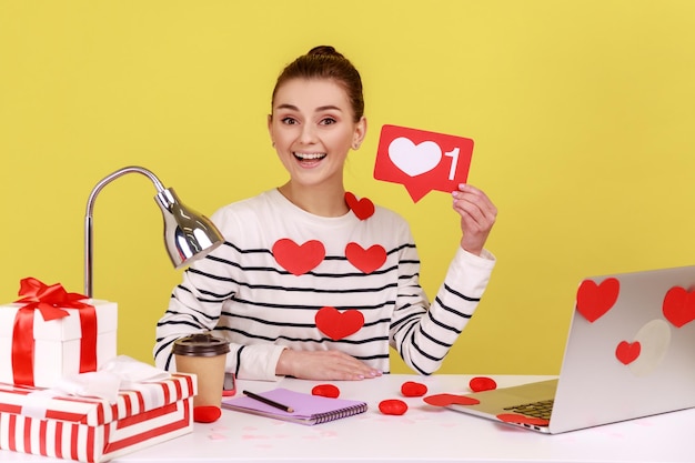 Woman holding like icon sitting at workplace covered heart sticks making post in social network