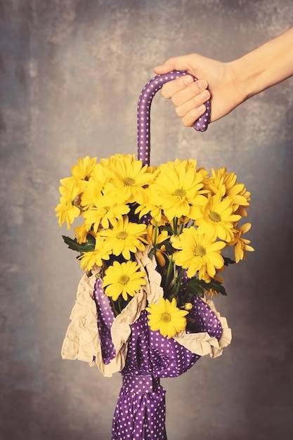 Woman holding lilac umbrella with beautiful flowers on gray wall background