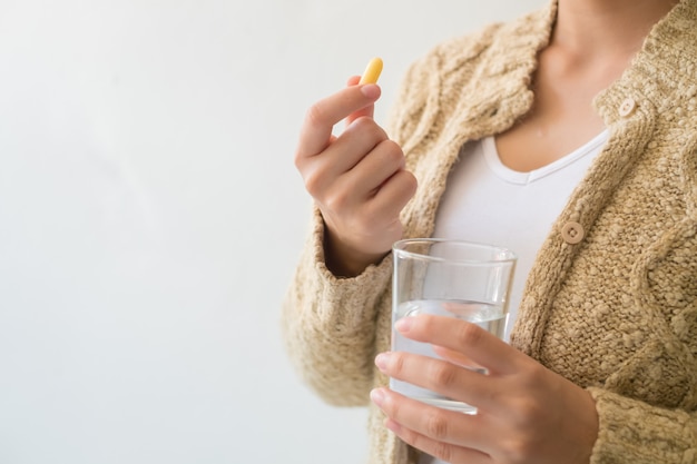 A woman holding a medicine and a glass of water in her hand. Medical and health concepts